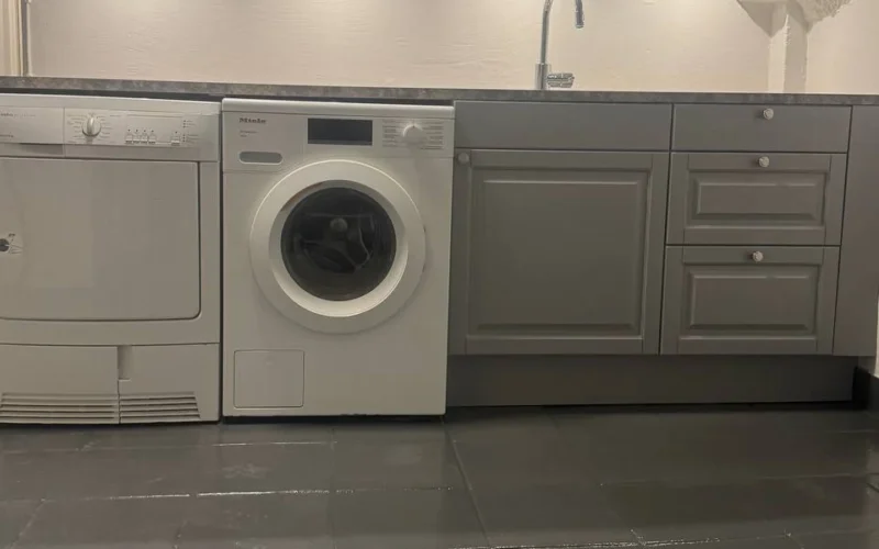 Renoverad tvättstuga med grå skåp, tvättmaskin och klinkergolv